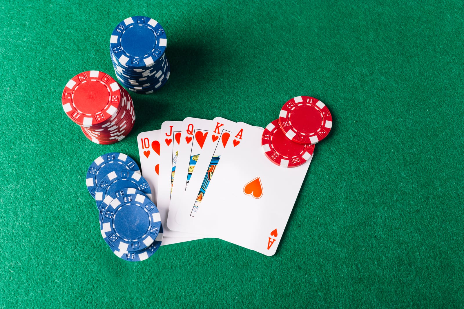 A royal flush of hearts with poker chips on green felt